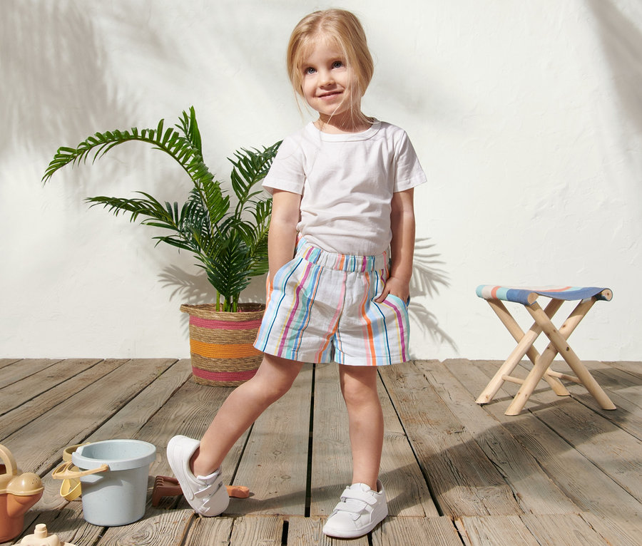 Mädchen steht auf einem Holzboden und trägt Web-Shorts.