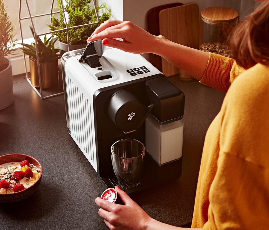 Frau öffnet eine weiße Cafissimo milk Kaffeemaschine und hält eine Kapsel.