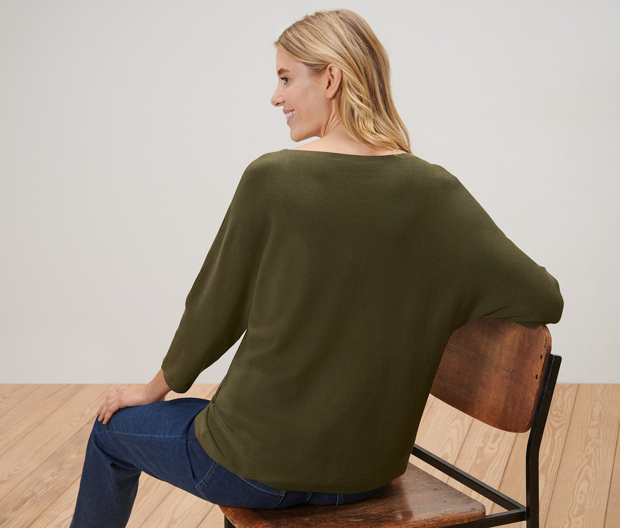 Frau sitzt auf einem Stuhl und trägt einen Feinstrickpullover.