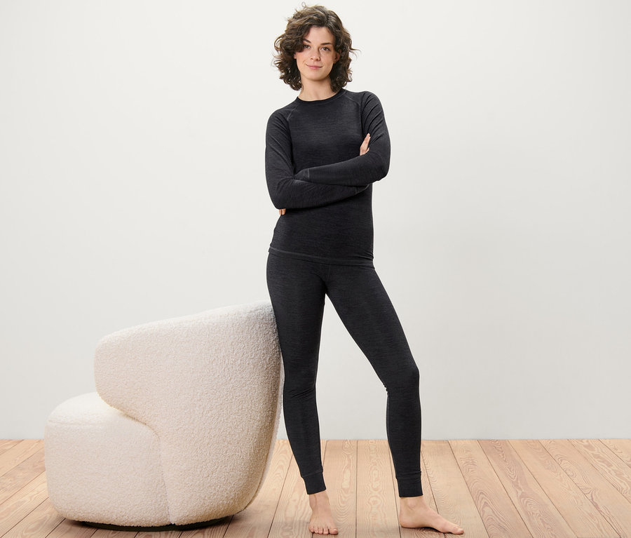 Frau posiert in langer Unterhose mit RWS-zertifizierter Wolle und Oberteil auf Holzboden neben einem cremefarbenen Sessel.