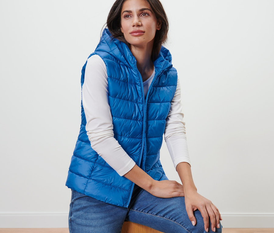 Frau sitzt und trägt eine blaue Steppweste mit Kapuze.