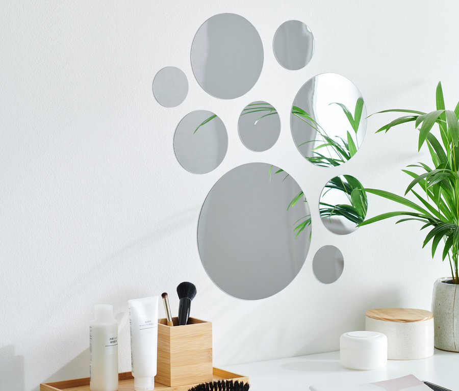 Neun selbstklebende Spiegelsticker sind kreisförmig auf einer weißen Wand über einem weißen Tisch angeordnet.