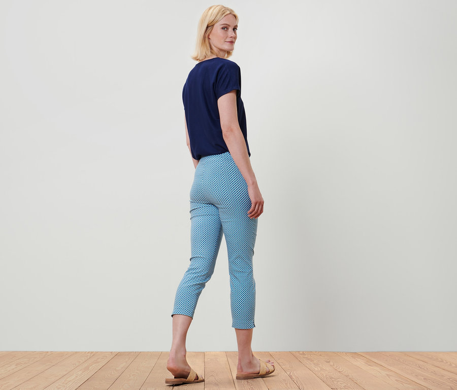 Frau blickt über die Schulter, trägt ein blaues T-Shirt und eine 7/8-Stretchhose mit Alloverprint.