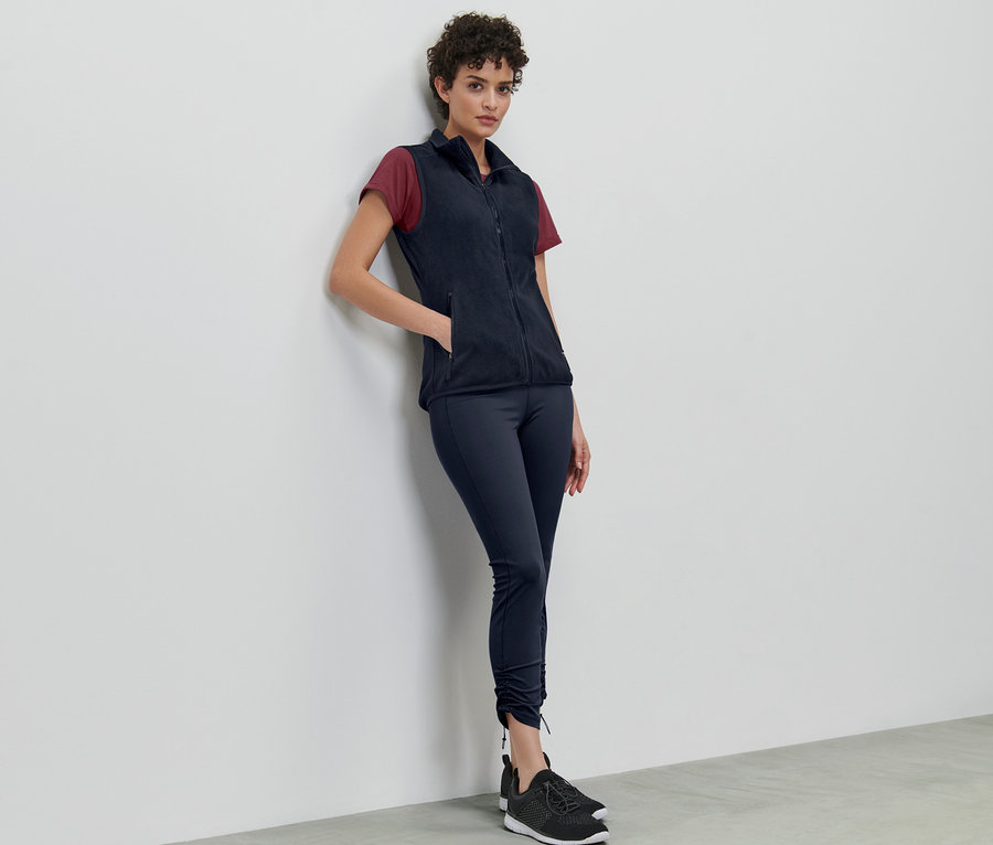 Frau lehnt an Wand und trägt eine Fleece-Weste.