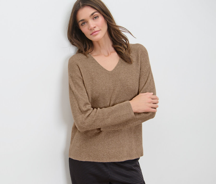 Frau an Wand gelehnt trägt camel Grobstrickpullover.