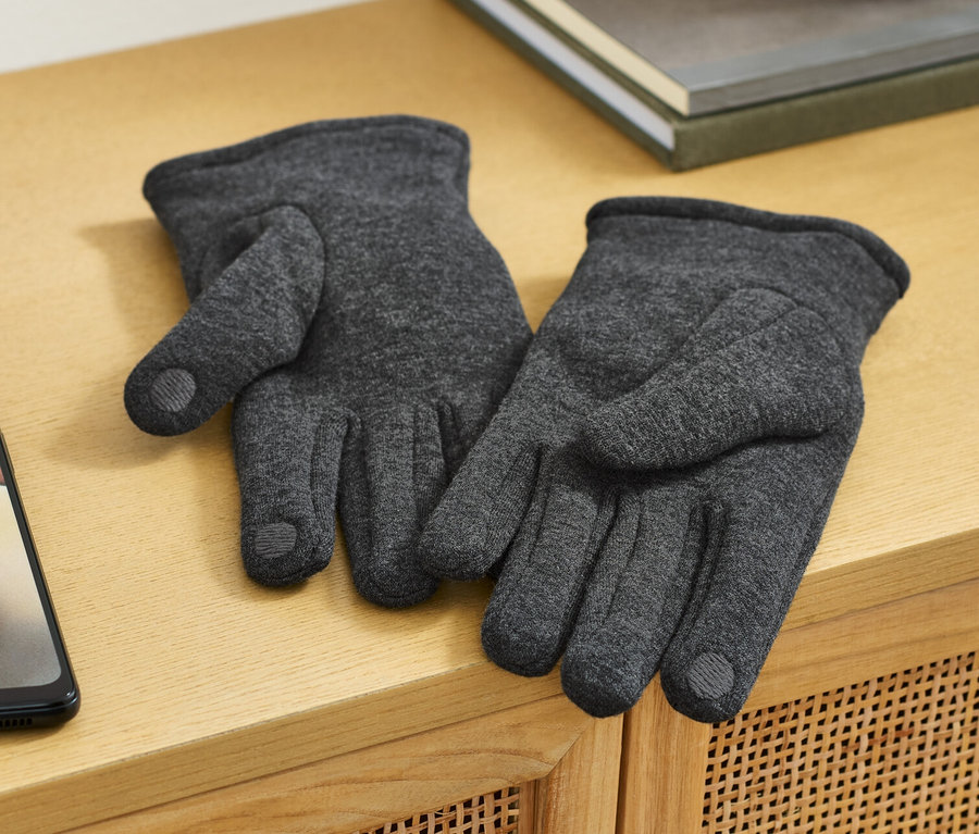 Zwei Sweathandschuhe liegen auf einer Holzkommode neben einem Handy.