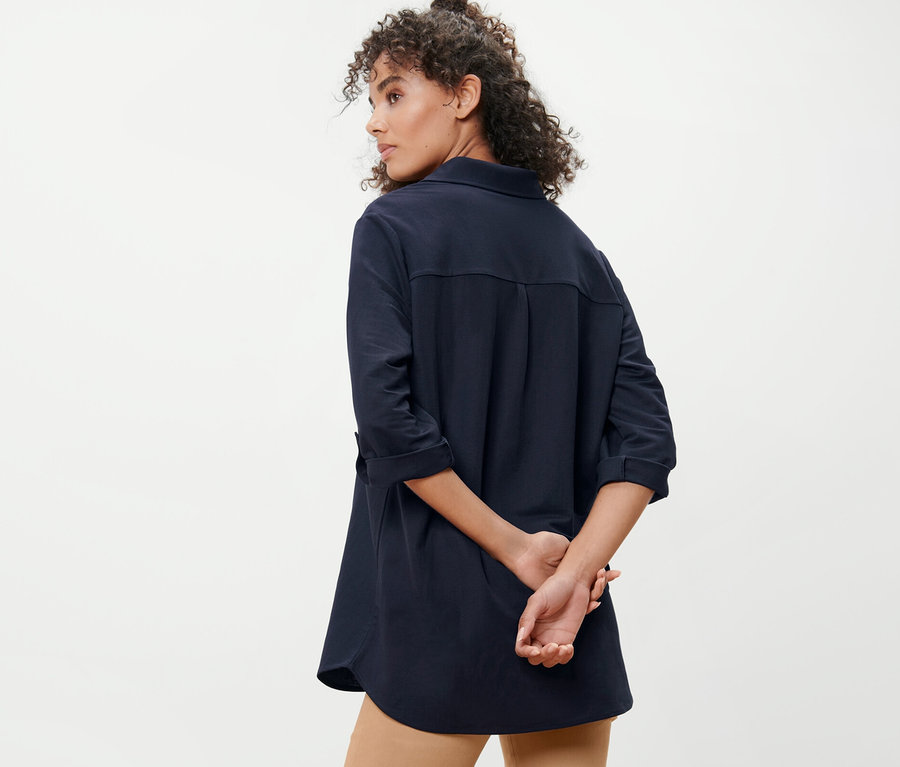 Frau posiert von hinten mit dunkelblauer Piqué-Jerseybluse.