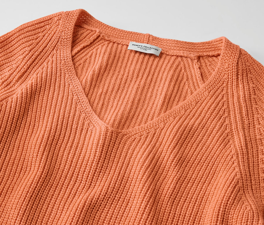 Detailansicht eines pfirsichfarbenen Strickpullovers mit V-Ausschnitt.