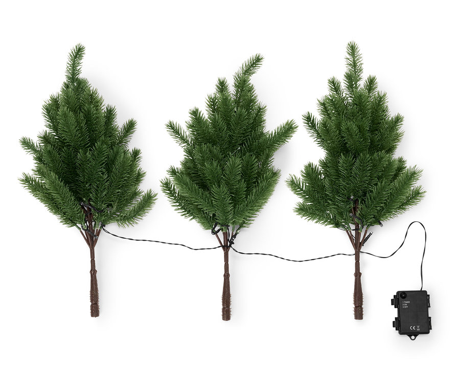 Drei kleine Weihnachtsbäume mit braunen Stämmen sind durch ein schwarzes Kabel verbunden, an dem ein schwarzes Netzteil befestigt ist.