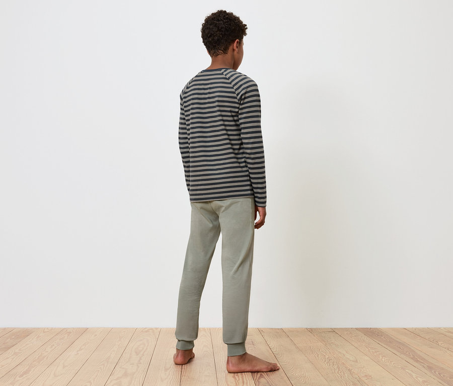 Ein Junge steht mit dem Rücken zum Betrachter und trägt ein grau-gestreiftes Langarmshirt und graue Jogginghose.