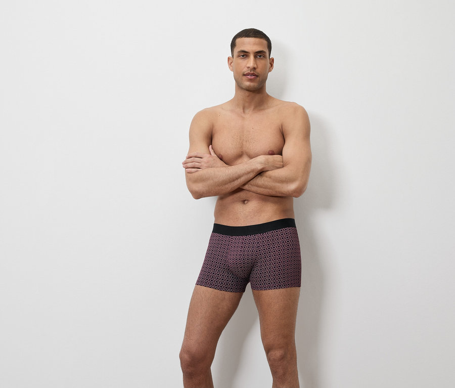 Mann posiert mit verschränkten Armen in Boxershorts mit geometrischem Muster.