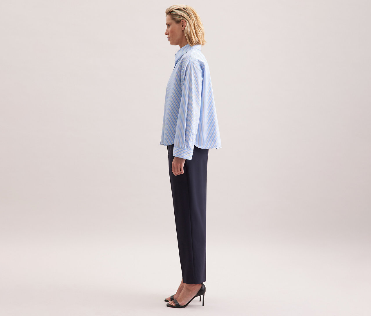 Frau von der Seite, die eine Seidensticker Oversize-Hemdbluse und dunkle Hosen trägt.