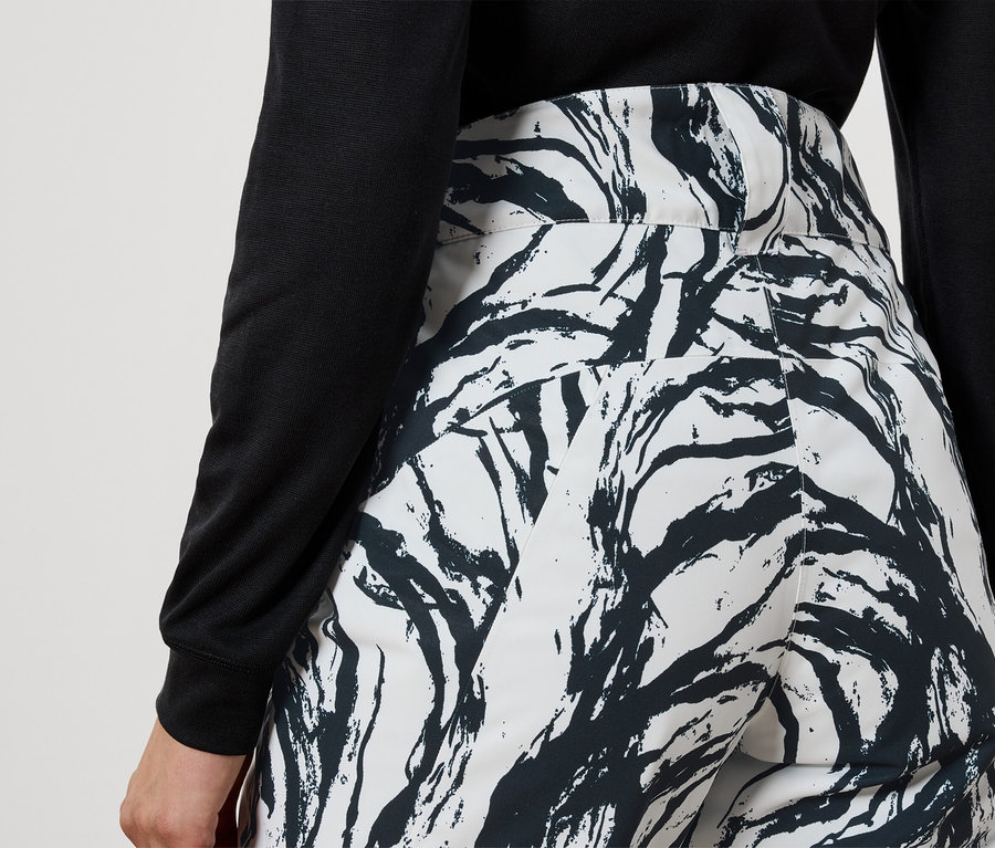 Rückansicht einer Frau mit schwarzem Oberteil und weisser Hose mit schwarzem Zweigmuster.