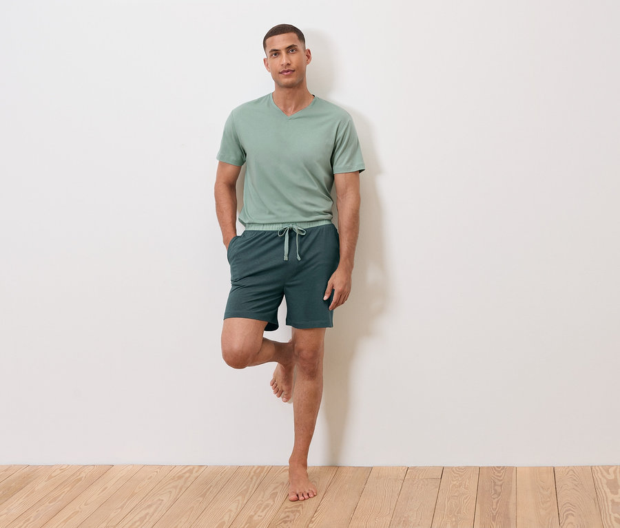 Mann steht auf einem Bein an einer Wand, trägt ein grünes T-Shirt und Shorts.