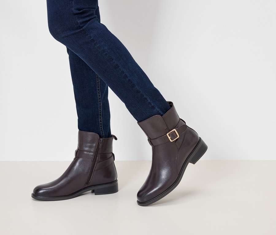 Beine in dunkelblauen Jeans und braunen Lederstiefeletten mit Schnalle und goldener Schließe.