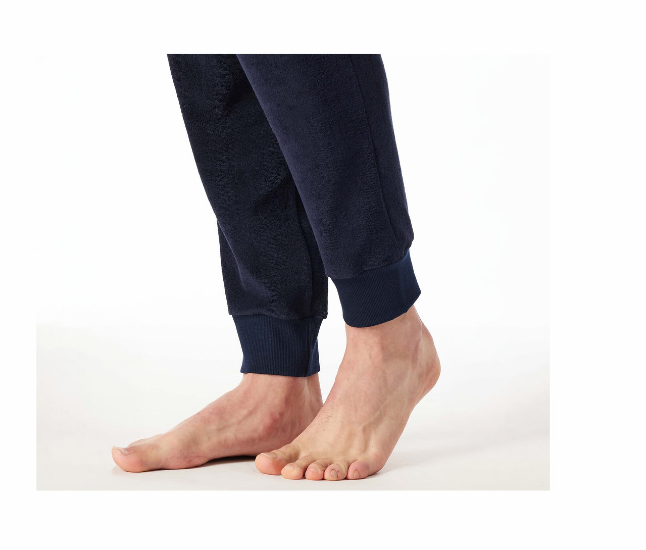 Füße und Unterschenkel einer Person in einer dunkelblauen SCHIESSER Frottee-Pyjamahose mit gerippten Bündchen auf weißem Hintergrund.