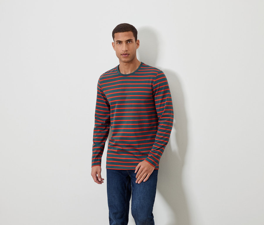 Mann steht und trägt ein langärmliges Streifenshirt und Jeans.