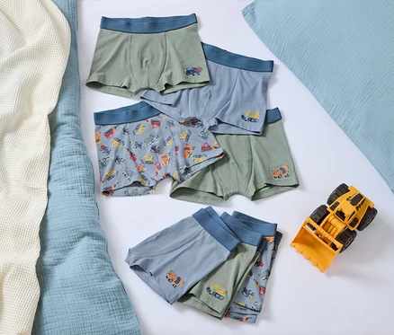 Auf einem Bett liegen mehrere Jungen-Boxershorts mit Automotiven und ein gelber Spielzeugbulldozer.