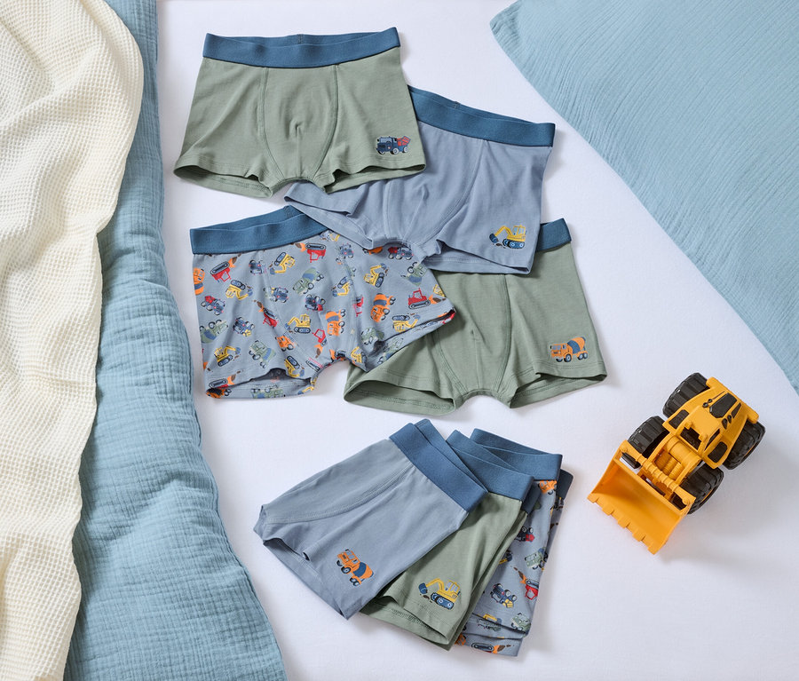 Auf einem Bett liegen mehrere Jungen-Boxershorts mit Automotiven und ein gelber Spielzeugbulldozer.