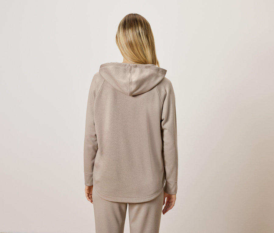 Frau trägt einen beigen Hoodie und eine Jogginghose, von hinten gesehen.