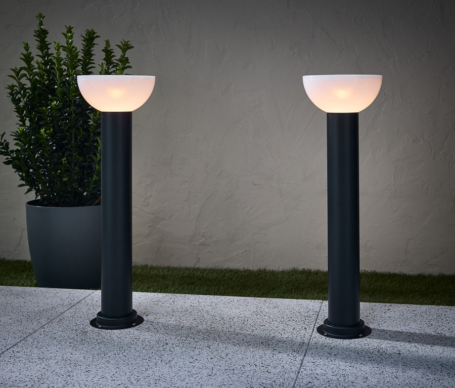 Zwei Solar-Wegleuchten beleuchten einen Weg. Neben einer Lampe steht ein Blumentopf.
