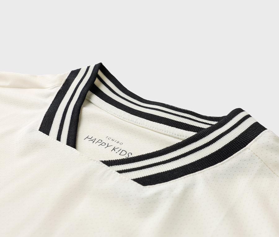 Detailansicht eines weißen T-Shirts mit einem schwarz-weiß gestreiften Kragen und dem 'TCHIBO HAPPY KIDS' Logo.