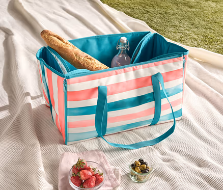 Picknickdecke mit gestreifter Kühltasche, Baguette, Wasserflasche, Erdbeeren und Oliven.
