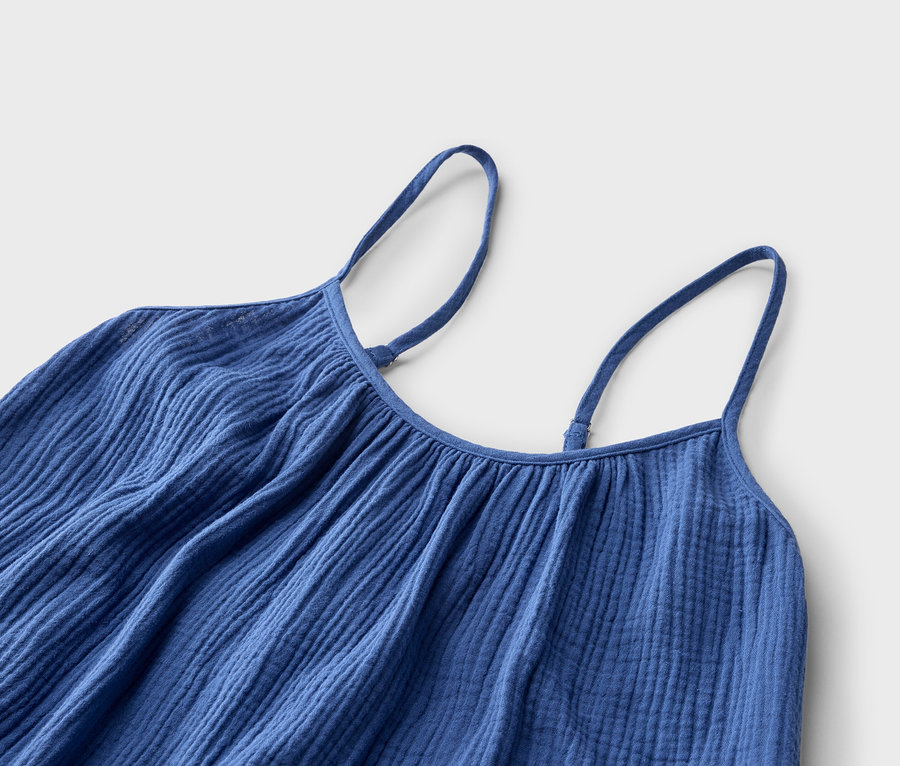 Nahaufnahme eines blauen Trägerkleids mit verstellbaren Trägern vor einem neutralen Hintergrund.
