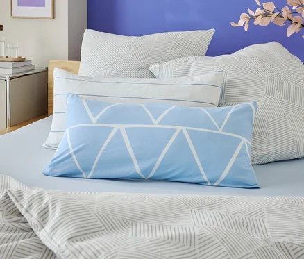 Nahaufnahme eines Bettes mit hellblauer Bettwäsche und mehreren Kissen mit geometrischen Mustern.