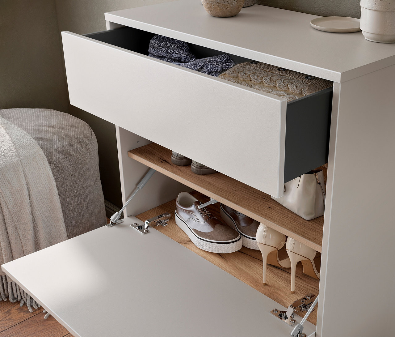 Offener Schuhschrank mit grauen Schuhen, Stiefeln und Handtasche auf Holzregalen. Eine Schublade oben ist teilweise geöffnet und zeigt Kleidung.