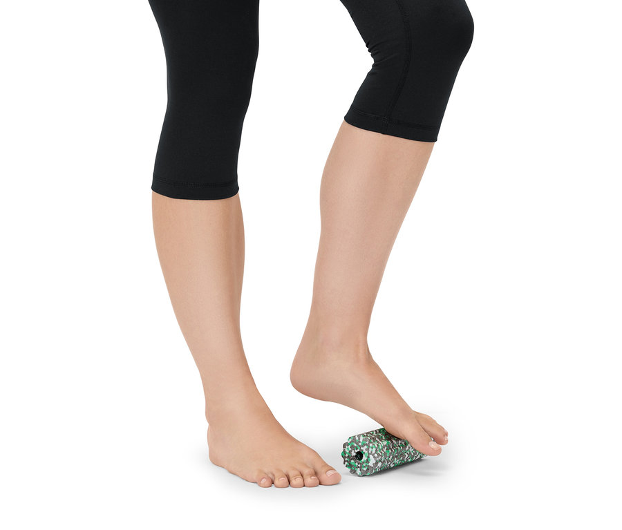 Frau in schwarzen Leggings rollt ihren Fuß auf einer grün-weiß gefleckten Schaumstoffrolle.