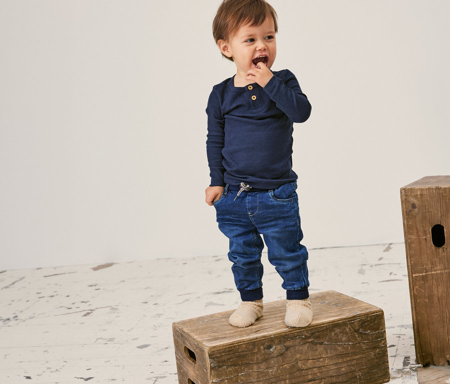 Kleinkind steht auf einer Holzkiste und trägt ein geripptes, langärmliges NAME IT Shirt in Dunkelblau.