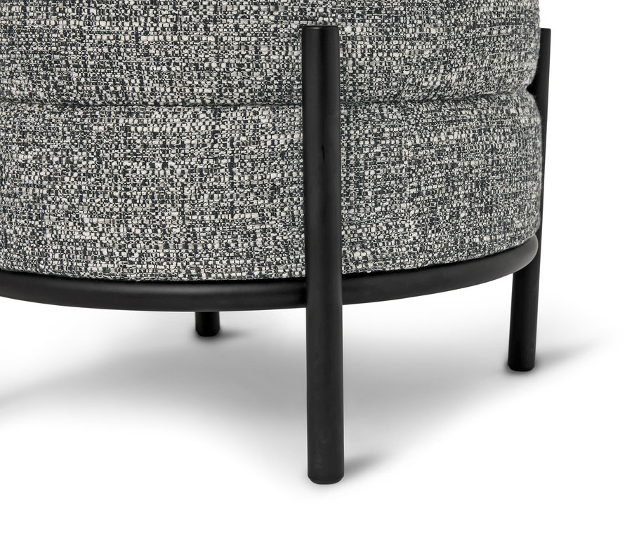 Nahaufnahme eines runden Hockers mit grau gemustertem Stoffbezug und schwarzen Metallbeinen.