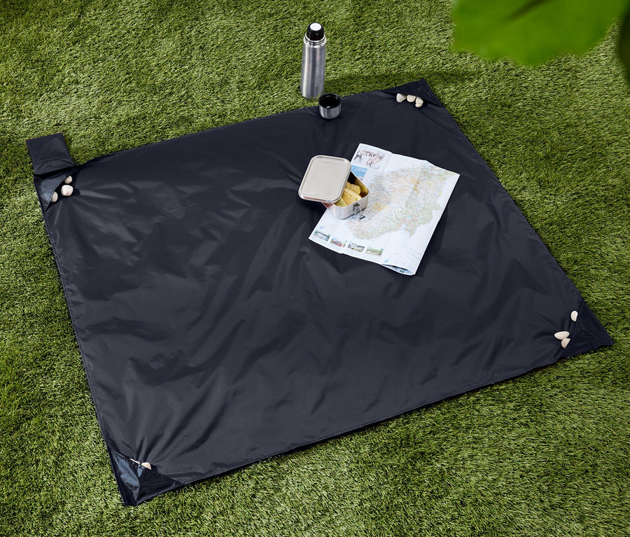 Dunkelblaue Picknickdecke mit Snacks, Thermoskanne und Karte auf einer grünen Grasfläche.