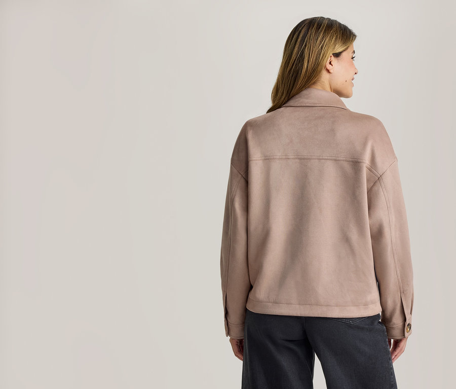 Frau von hinten, trägt eine hellbraune Kragenjacke in Wildleder-Optik und dunkle Hose, blickt nach rechts.