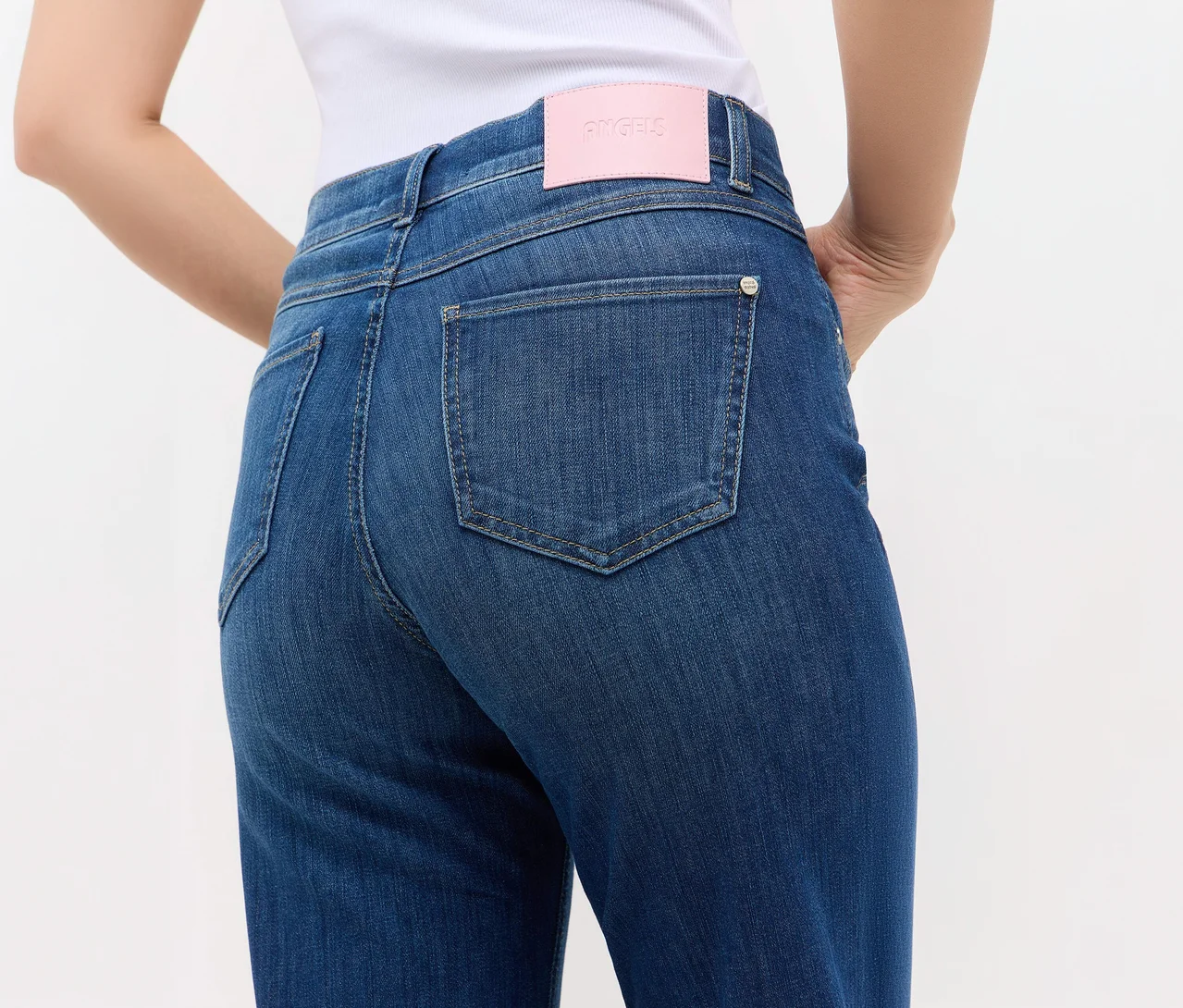 Rückenansicht einer Person in blauen Jeans mit rosa ANGELS-Etikett am Bund und sichtbaren Gesäßtaschen. Ein weißes Oberteil ist ebenfalls zu sehen.