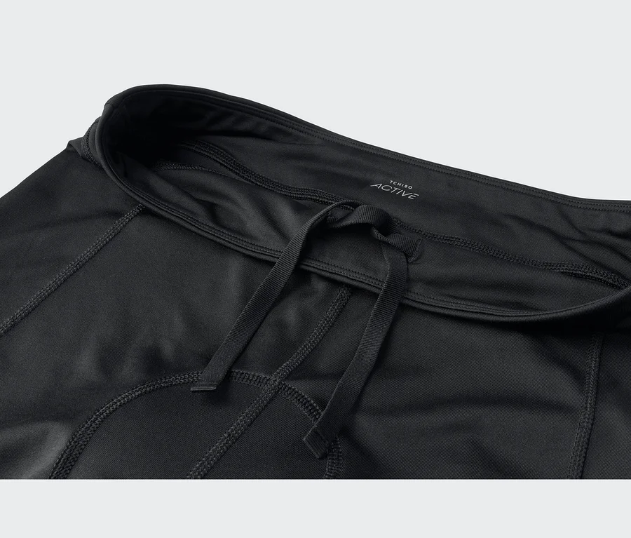Schwarze Sportbekleidung mit Kordelzug am Bund und sichtbaren Nähten. Ein Etikett zeigt "TCHIBO ACTIVE".