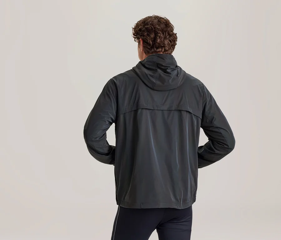 Person von hinten in einer dunkelgrauen Kapuzenjacke mit Händen in den Taschen und dunklen Hosen.