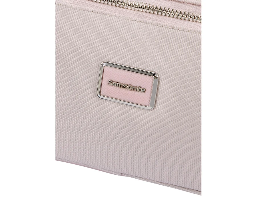 Nahaufnahme eines hellrosa strukturierten Stoffartikels mit einem silbernen Reißverschluss oben und einem rechteckigen, silbergerahmten Samsonite-Logo-Schild mit hellrosa Hintergrund.