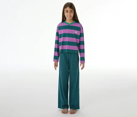 Mädchen lächelt, trägt einen SCHIESSER Kinder-Pyjama mit lila-grün gestreiftem Langarmshirt, grüner Hose und hat nackte Füße.