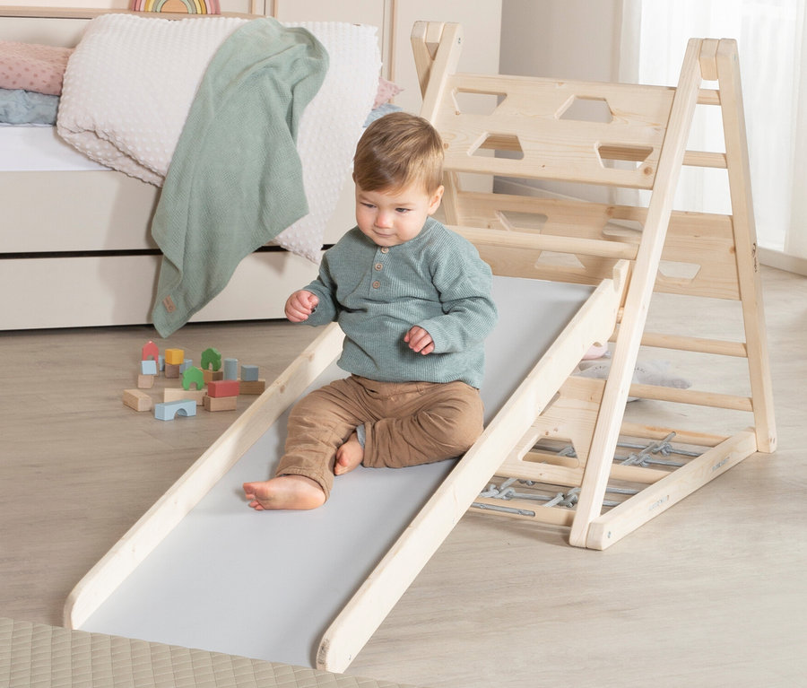 Ein Kind rutscht auf der grauen roba Rutschbrett Rutsche herunter, im Hintergrund Holzspielzeug und ein Bett.