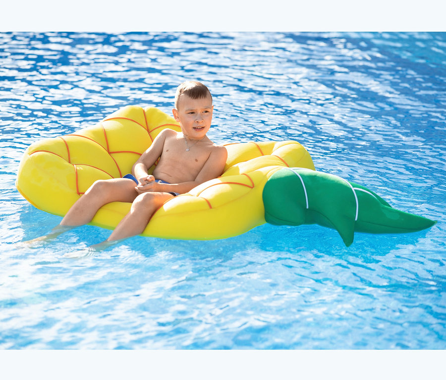 Junge sitzt auf aufblasbarer Pool Buddy Ananas im Pool.
