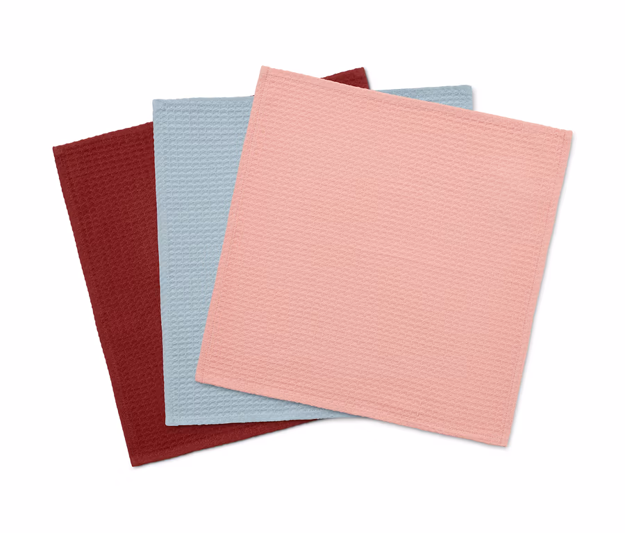 Drei Küchenhandtücher liegen übereinander: eines ist bordeauxrot, eines hellblau und eines rosa.