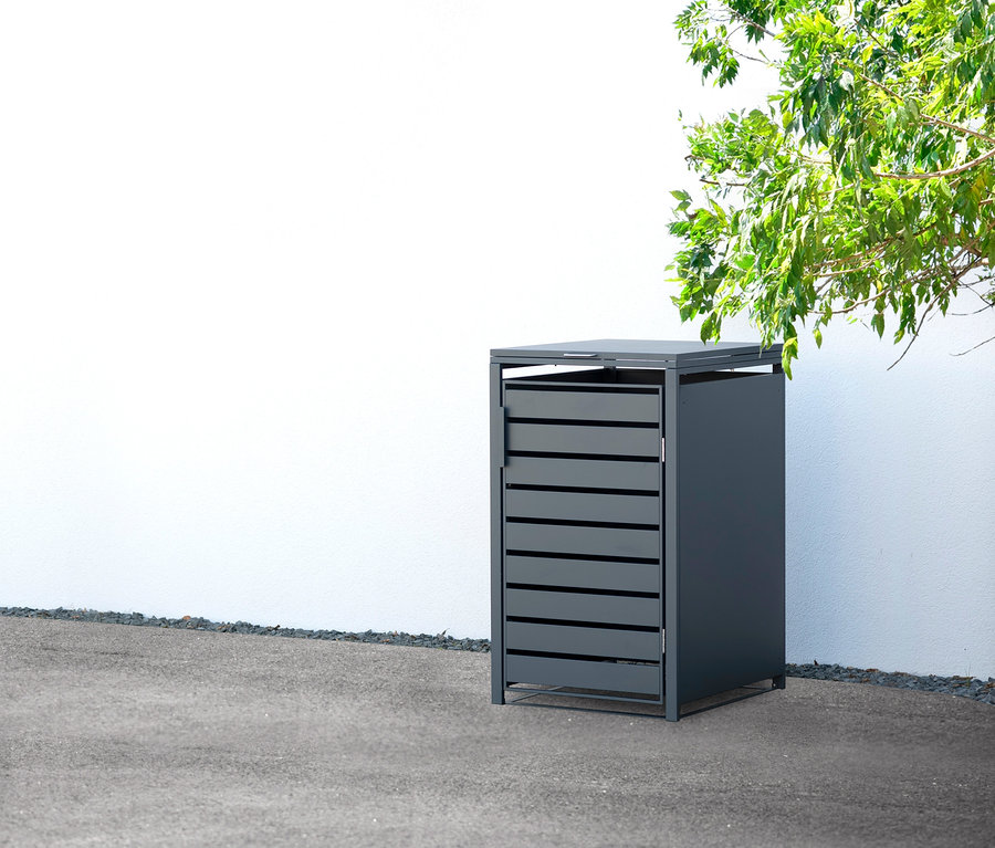 Eine graue Mülltonnenbox aus Stahl steht draußen an einer weißen Wand.