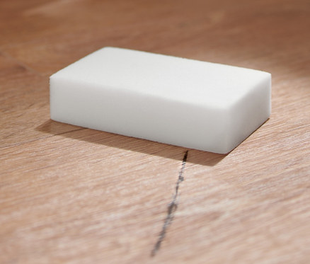 Ein 10er-Pack Schmutzradierer liegt auf einem Holzboden neben einem beigen Hocker.
