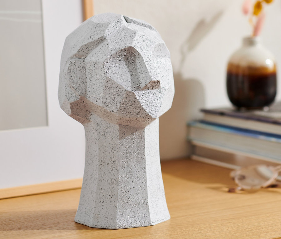Eine graue Deko-Skulptur in Kopfform auf einem Holztisch.
