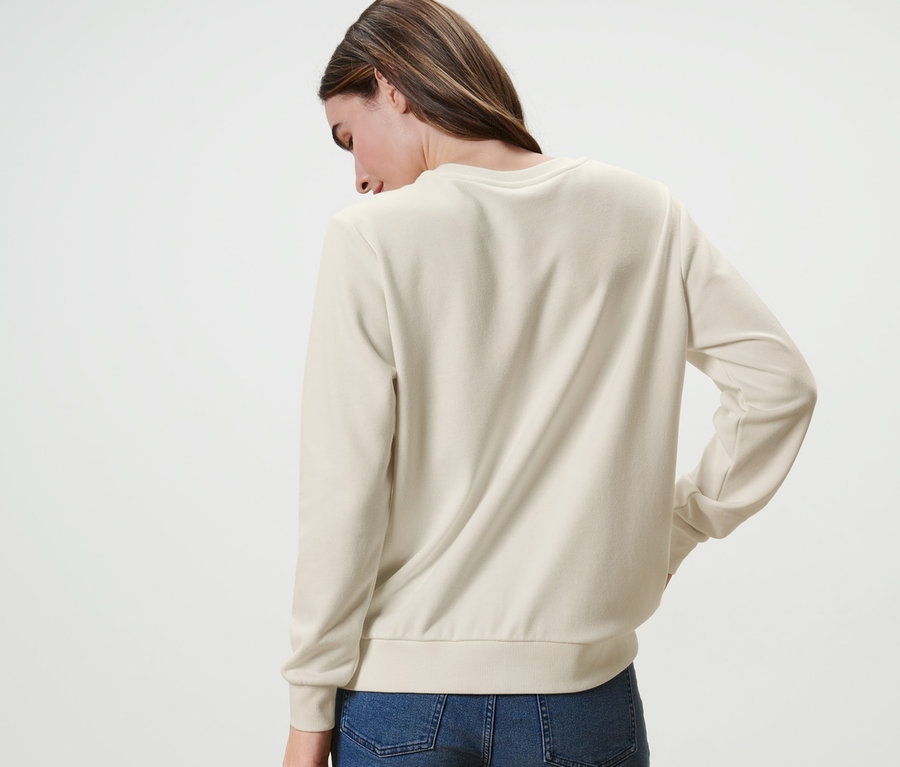Eine Frau mit dem Rücken zur Kamera trägt ein Sweatshirt mit Stickerei und Jeans.