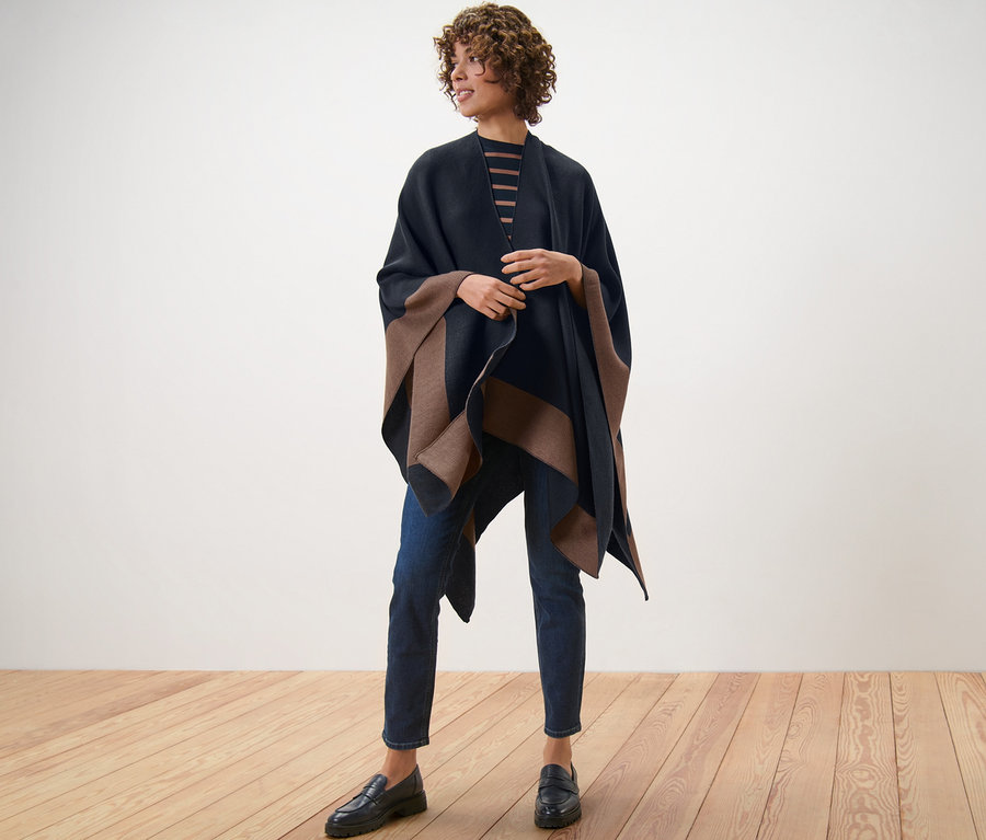 Eine Frau steht auf einem Holzboden und trägt einen Wende-Poncho.