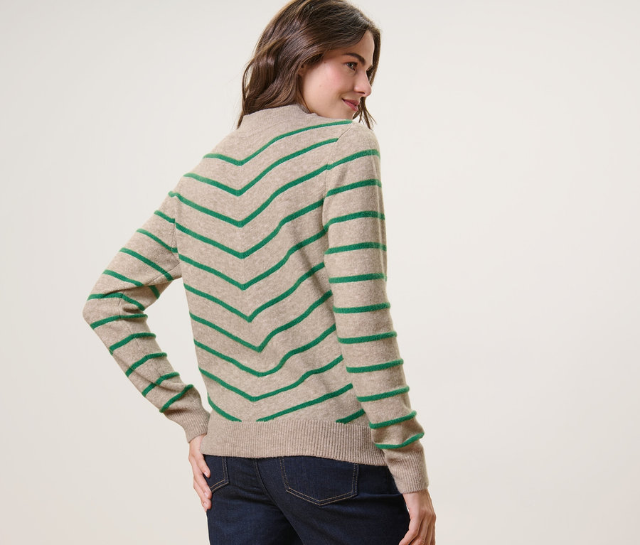 Frau blickt über die Schulter und posiert in einem gestreiften Strickpullover mit Stehkragen in Creme.