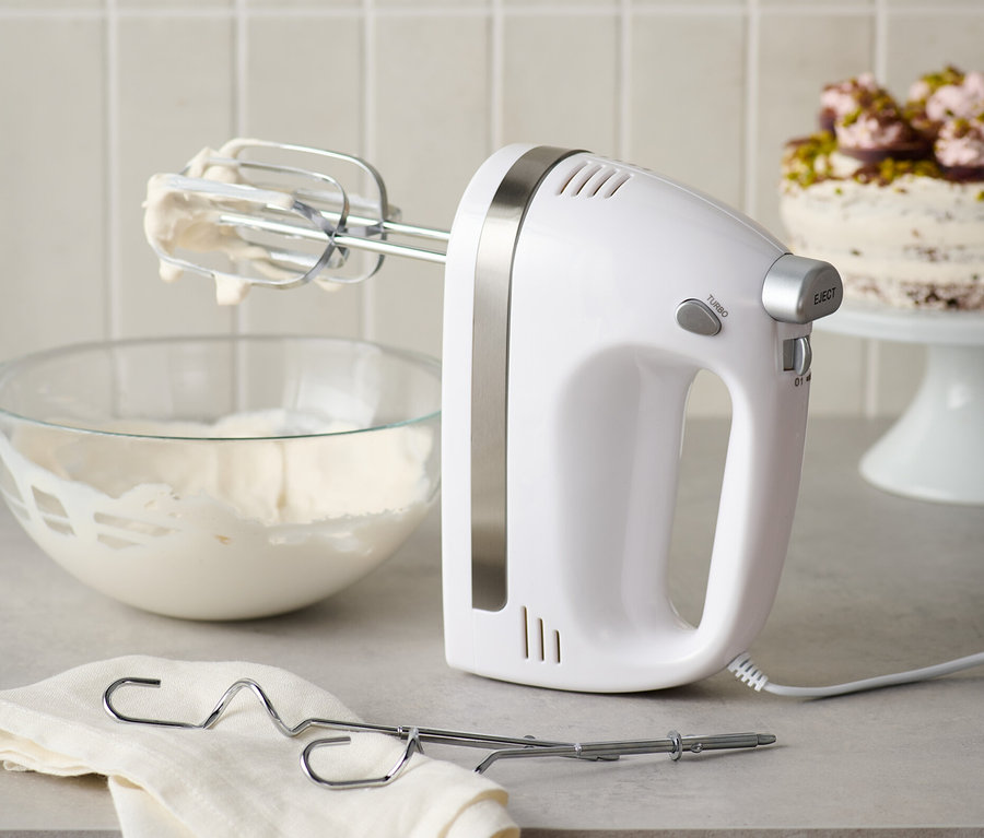Ein weißer Handmixer mit Edelstahl-Quirlen steht neben einer Schüssel mit Schlagsahne und einem Tuch.